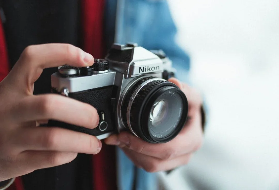 Original photo — Nikon SLR camera vector line drawing, lens barrel with focus ring, pentaprism viewfinder and top-plate control dials.